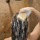 Person washing hair with a shampoo bar in a shower.