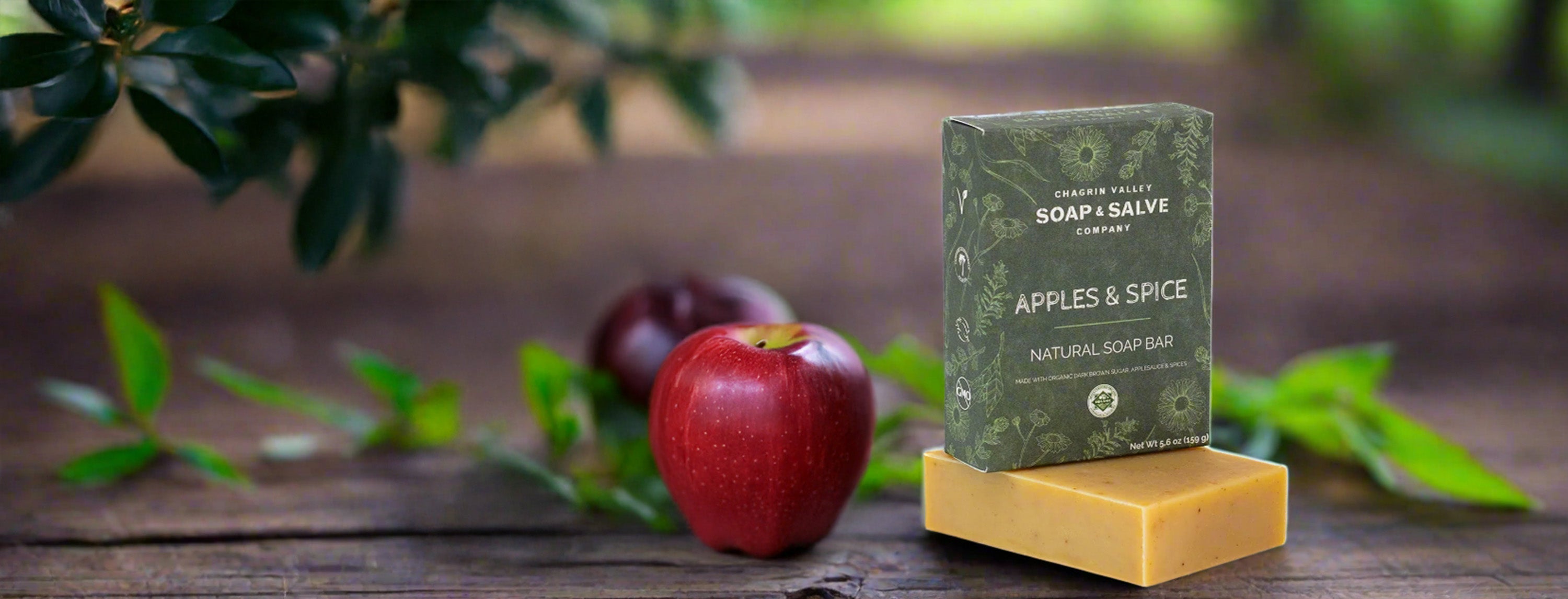 Bar of soap on a wooden stand with an apple and plums on a rustic wooden surface.