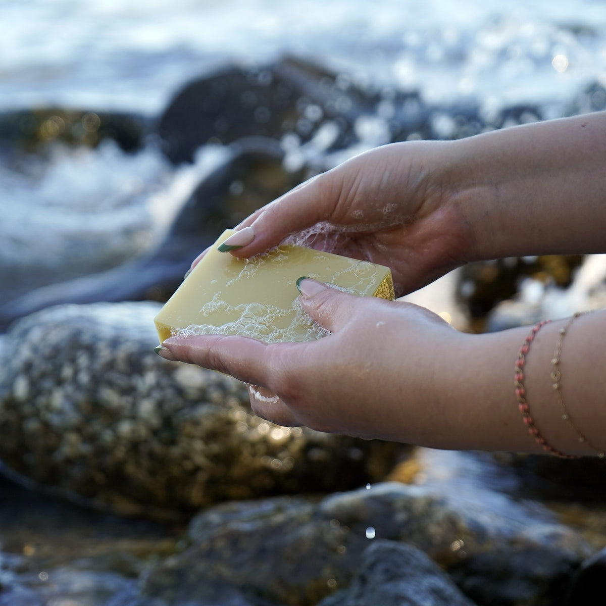Wet hands working up a light lather with an unscented Castile & Cocoa soap bar by the water